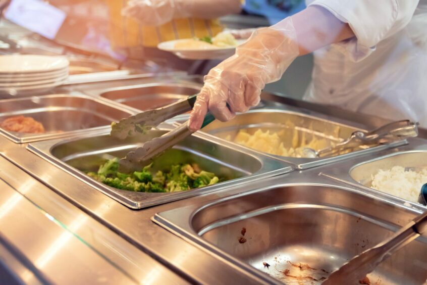Image shows school chef reaching into lunch line to illustrate School meal awards
