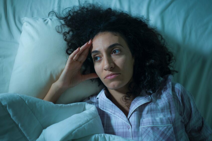 Woman going through physical symptoms of grief lying awake in bed looking sad and contemplating her future