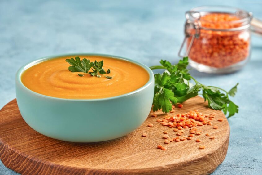 Red lentil soup sitting in a bowl on a table with a container of lentils next to it