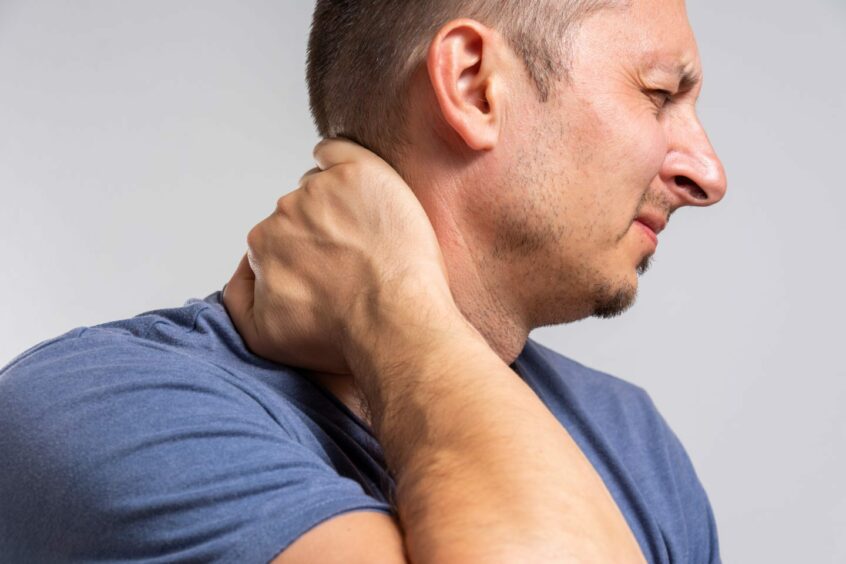 Man experiencing physical symptoms of grief holding onto his stiff neck in discomfort 
