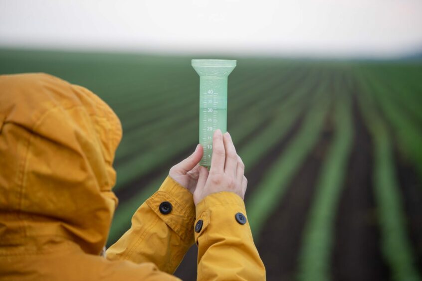 Woman standing on farm lands holding an empty rain gauge hoping its going to be filled amid dry weather