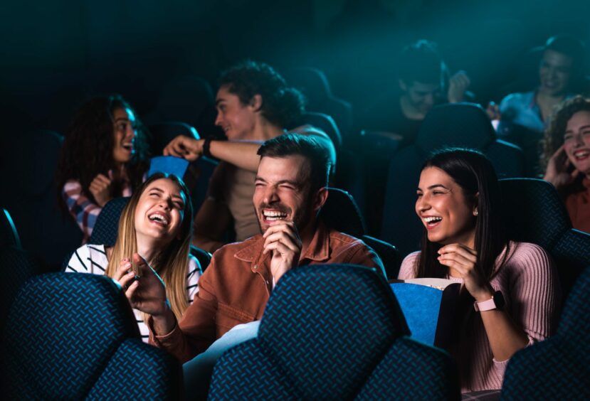 Group of cheerful people laughing while watching movie in cinema.