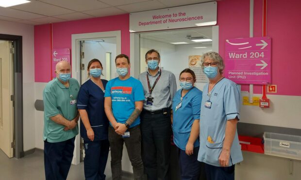 Lee Findlay and the staff who care for him.  Left to Right: David Birnie (receptionist), Claire McNab (Senior Charge Nurse), Mr Findlay, Dr Carl Counsell (consultant neurologist), Ocean Smith (staff nurse), David Henderson (HCSW).. Aberdeen Royal Infirmary . Supplied by NHS Grampian.