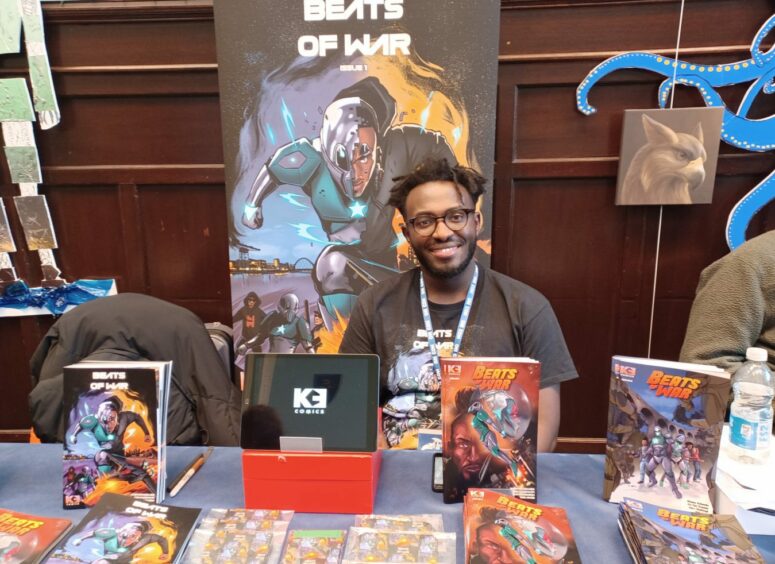 Comics writer Etienne Kubwabo sits behind a table displaying his comics.