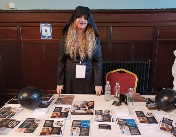 A woman in fancy dress runs the UHI stall at OH!CON.