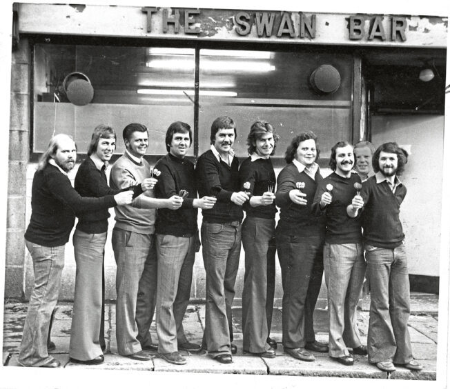 An aberdeen darts team pose in a line with darts in their right hands.