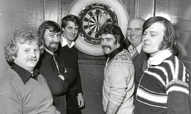 A darts team posing in front of a dart board