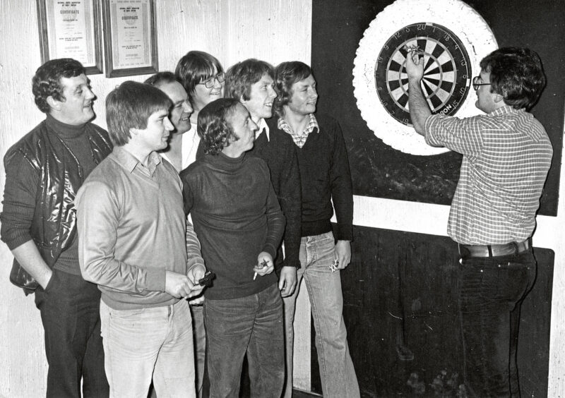A man counts the sore on the dart board as the rival team watches.