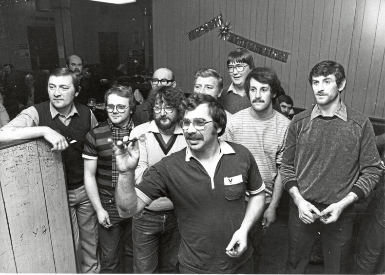 Two Aberdeen darts teams watch as one member prepares to throw a dart.