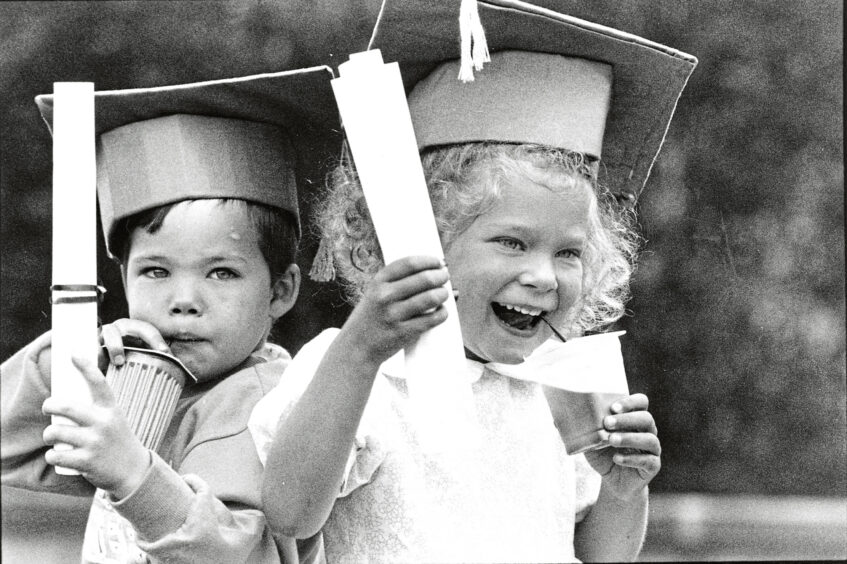 Two nursery pupils with graduation caps on and certificates in their hands