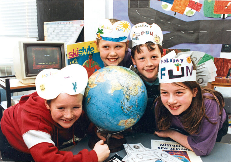 Four pupils with paper hats on posing with a globe