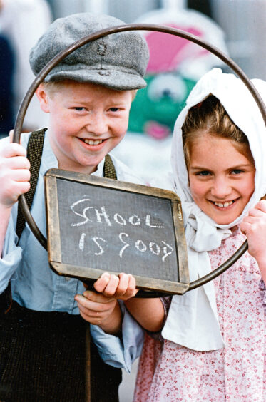 Two pupils in Victorian costumes holding a sign reading "School is good"