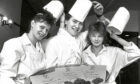 Three students with certificates on a platter taking their chef hats off