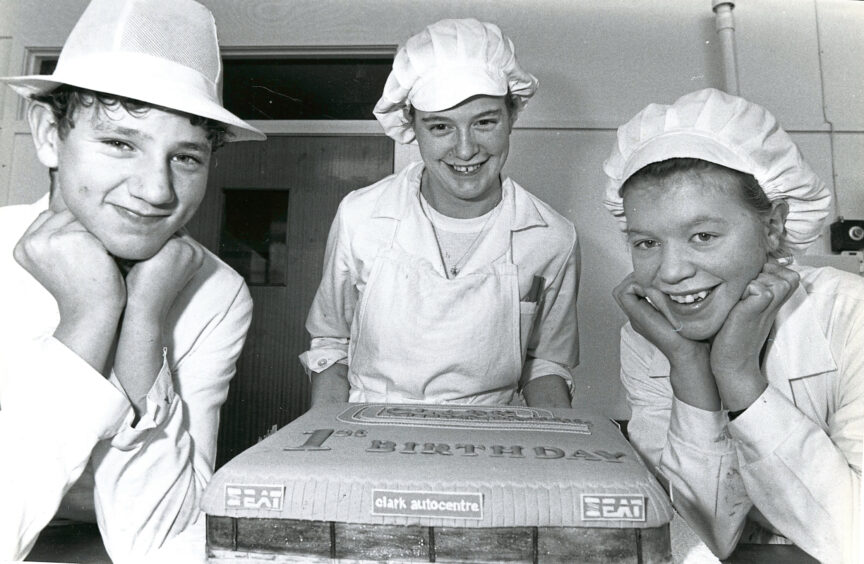 Three students smiling at the camera with a cake they baked and decorated