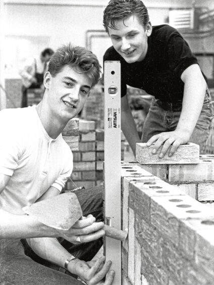 Two young men building a brick wall