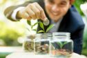 man in suit puts money in glass jar with young plant