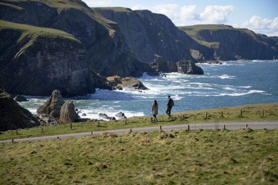 tourists look at stunning view of sea and mountains in Scotland