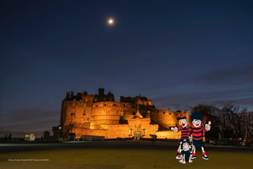 Minnie, Dennis and Gnasher pose in front of Edinburgh Castle at night - a picture perfect spot for family days out in Scotland