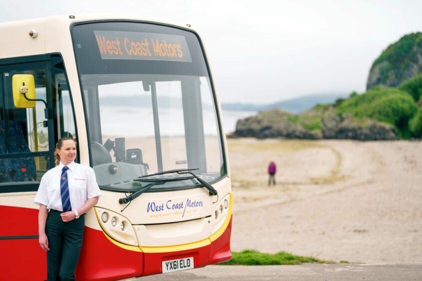 West Coast Motors staff member poses with a company bus parked near a beach