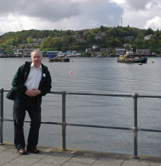 Jim Bruce who has a hernia that looks him in 'so much pain' standing on a rail with the sea behind him 