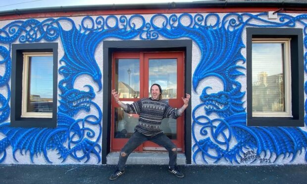 Dirk Robertson standing outside SIBC building with the blue dragon mural he painted on it