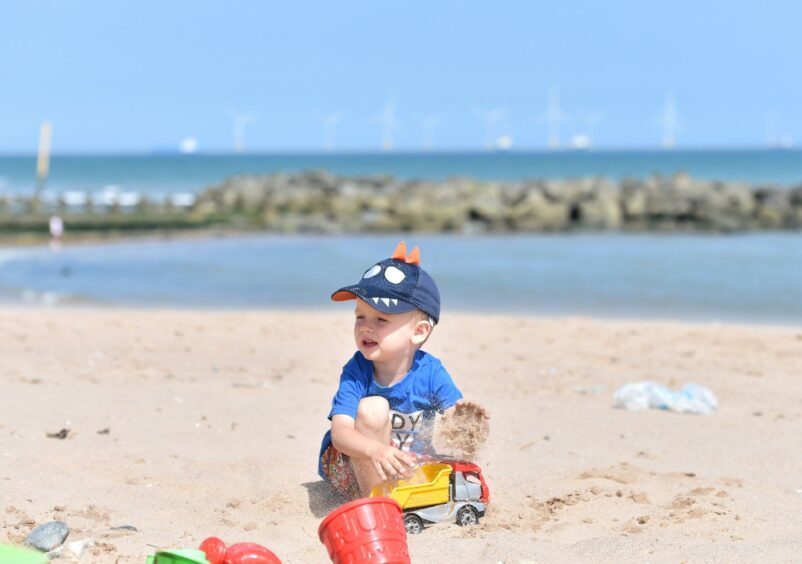 A young boy plays in the sand on Aberdeen beach. he has a red and green bucket and yellow and red tipper truck. 