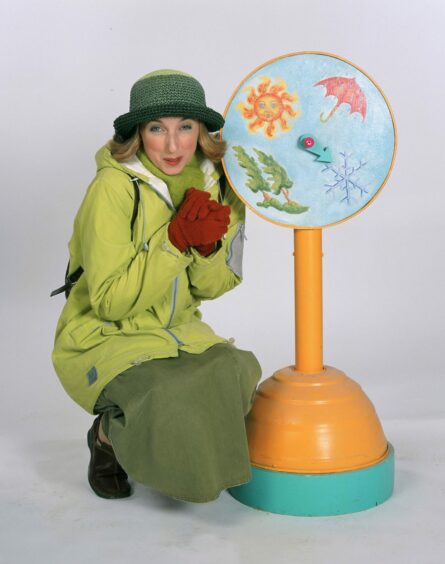 Miss Hoolie, portrayed by Julie Wilson Nimmo, crouching next to a weather wheel prop from Balamory