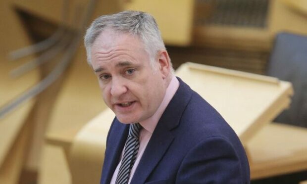 Richard Lochhead standing up speaking in the Scottish parliament building (Holyrood)