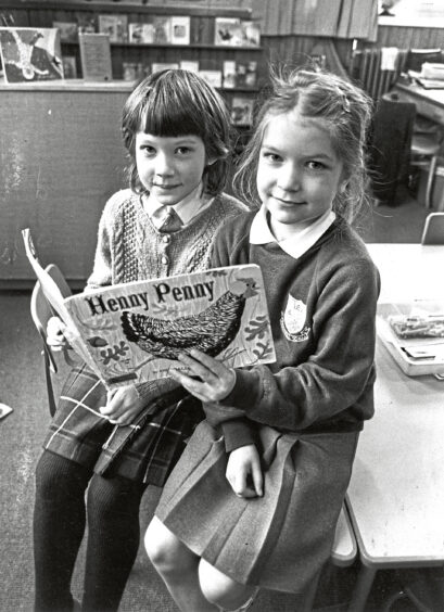 Two young girls reading a book together in a classroom