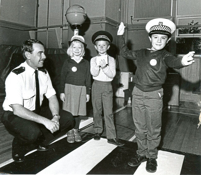 A policeman crouching next to three pupils learning to cross the road safely
