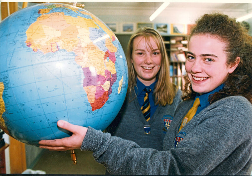 Two pupils smiling at the camera, the girl closest to the camera holds up a globe