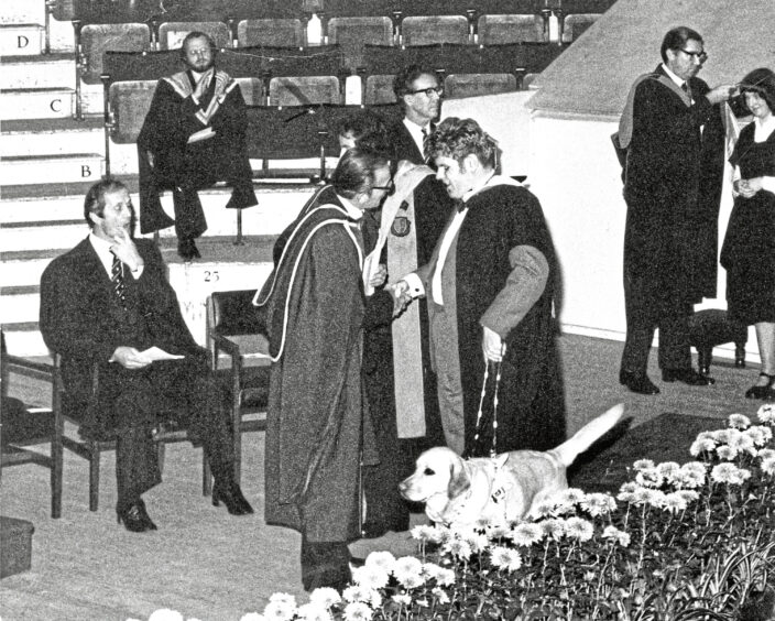 A blind student with his guide dog receiving his certificate