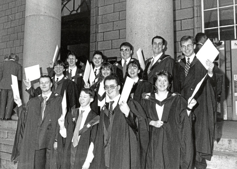 A group of graduates standing on steps, holding their certificates in the air