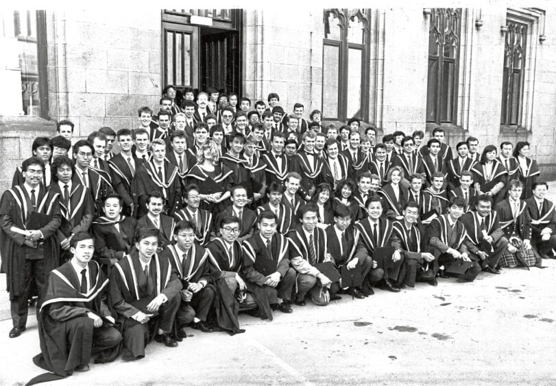 A large crowd of graduates stand on the stairs of Mitchell Hall, posing for a photo.