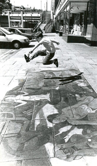 A young boy jumping over a work of art drawn out on the pavement on St Nicholas Street Aberdeen