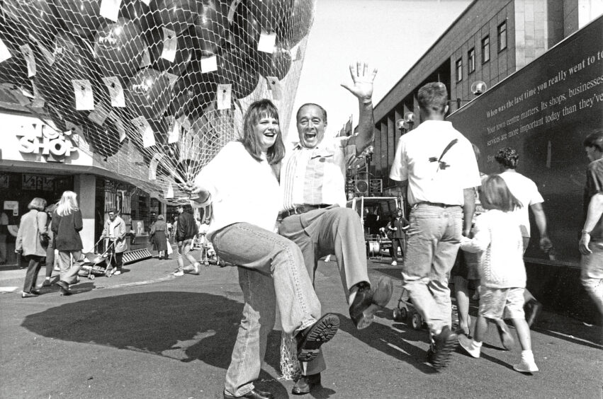 A man and woman grinning at the camera with a large net of balloons in the woman's hand