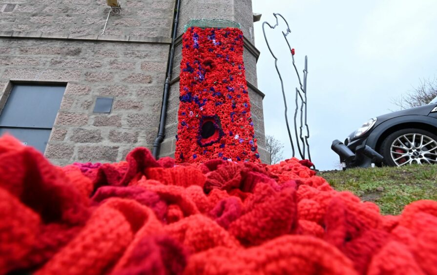 Knitted poppies attached to the wall of Victoria Hall in Ellon, draping toward the ground and meeting the camera in a Remembrance day display.