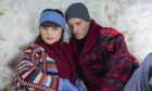 Stylish couple sitting in snow wearing luxury cashmere from Johnstons of Elgin.