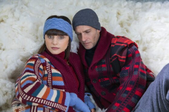 Stylish couple sitting in snow wearing luxury cashmere from Johnstons of Elgin.