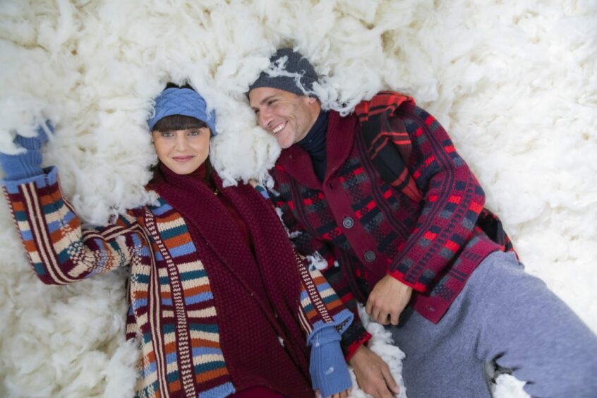 Couple lays in snow wearing Johnstons of Elgin