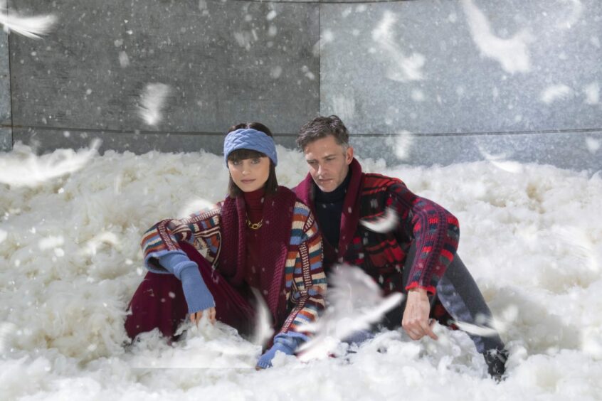 Couple wearing luxury cashmere gifts sit in snowfall.