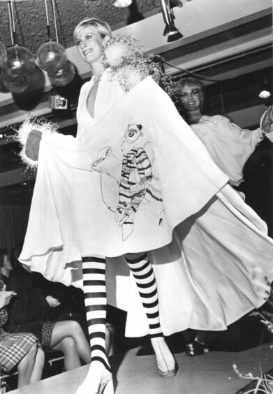 A model holding the skirt of her white dress up to show off black and white stiped tights. 