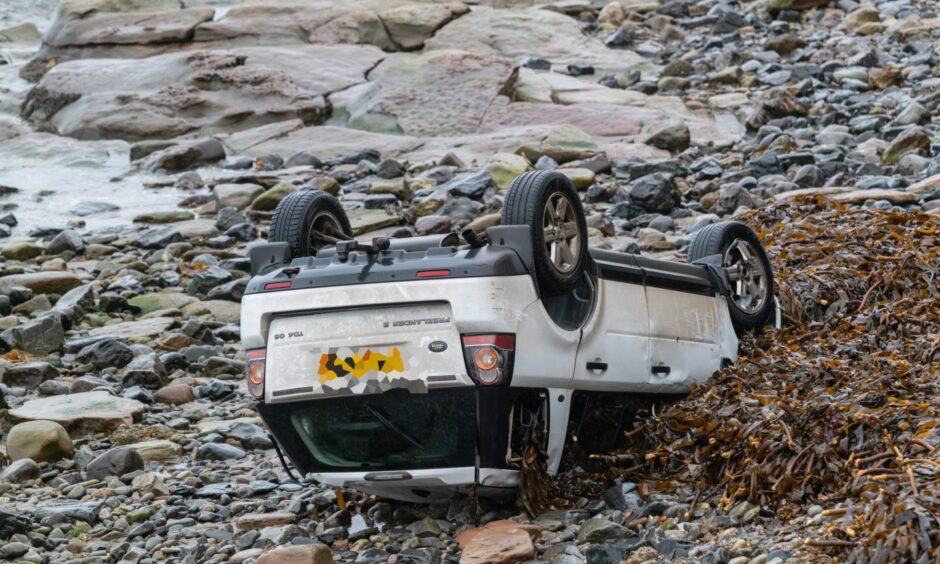 White Land Rover on its roof on Gardenstown beach