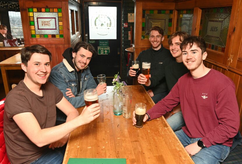 Five men sat around a table in a pub holding beers