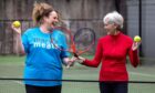 Judy Murray and Suzy Harley on a tennis court with racquets, lookig at each other and smiling