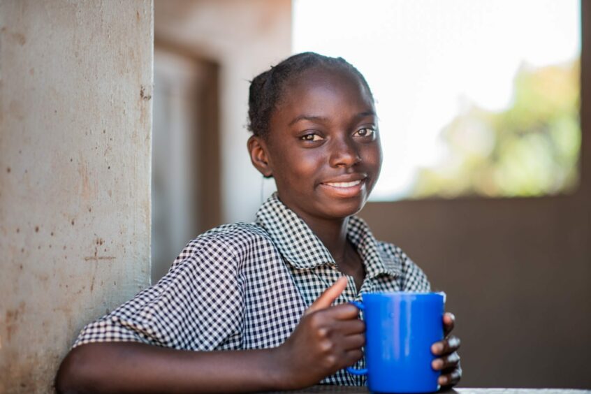 Ketty, 13, sitting outside a building in Africa with a blue mug