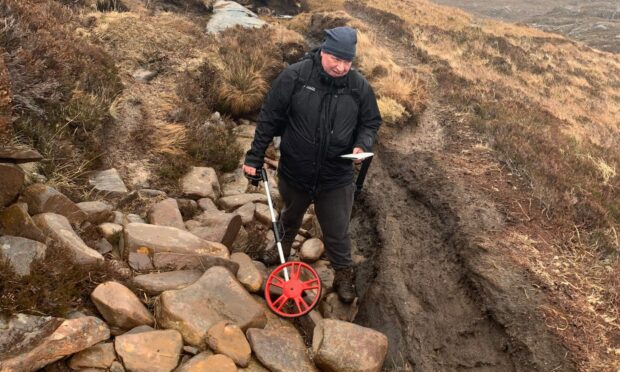 A man measuring rocks and recording the state of the path on An Teallach.