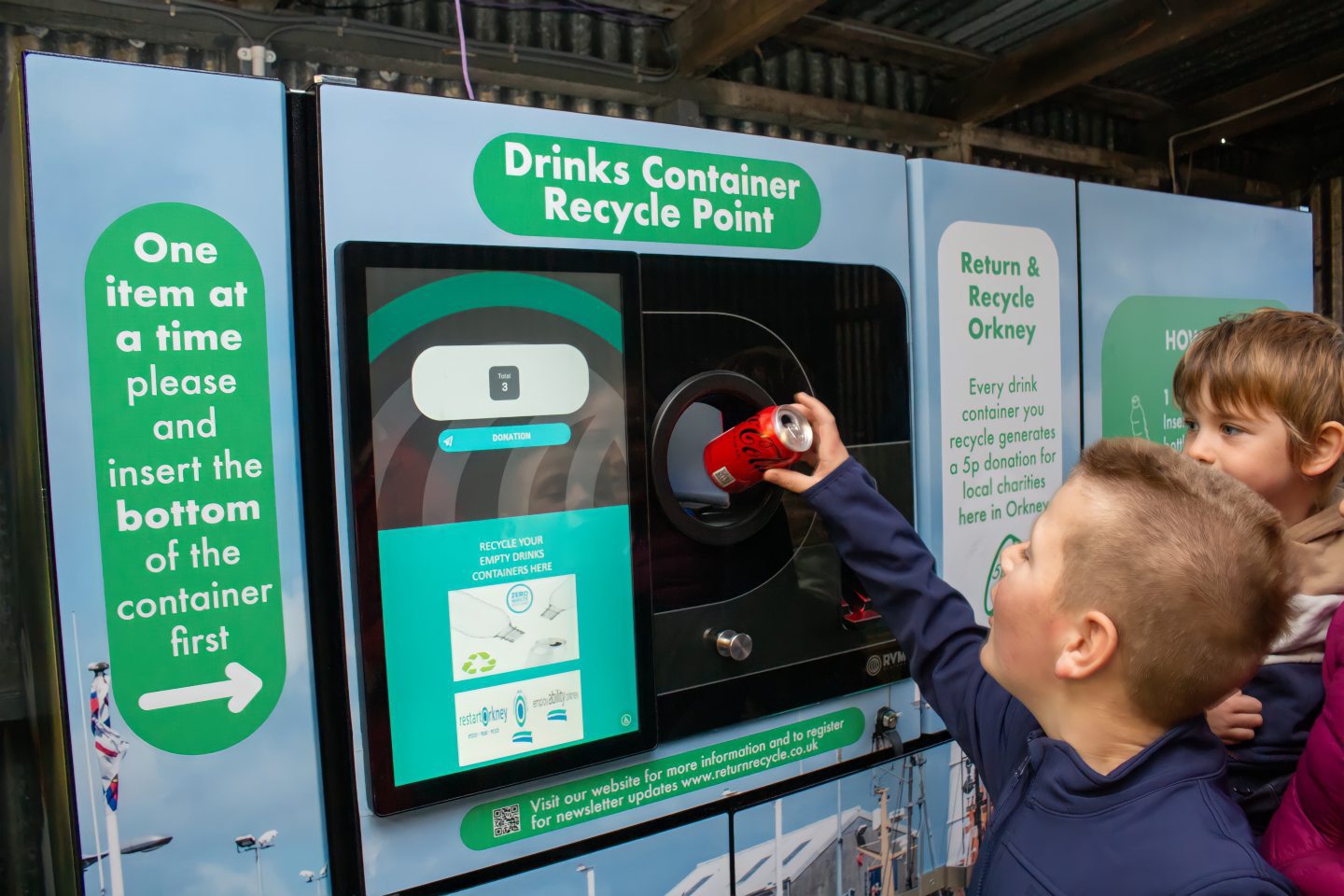 A child placing a can through the reverse vending machine as part of the Return and recycle Orkney pilot. 