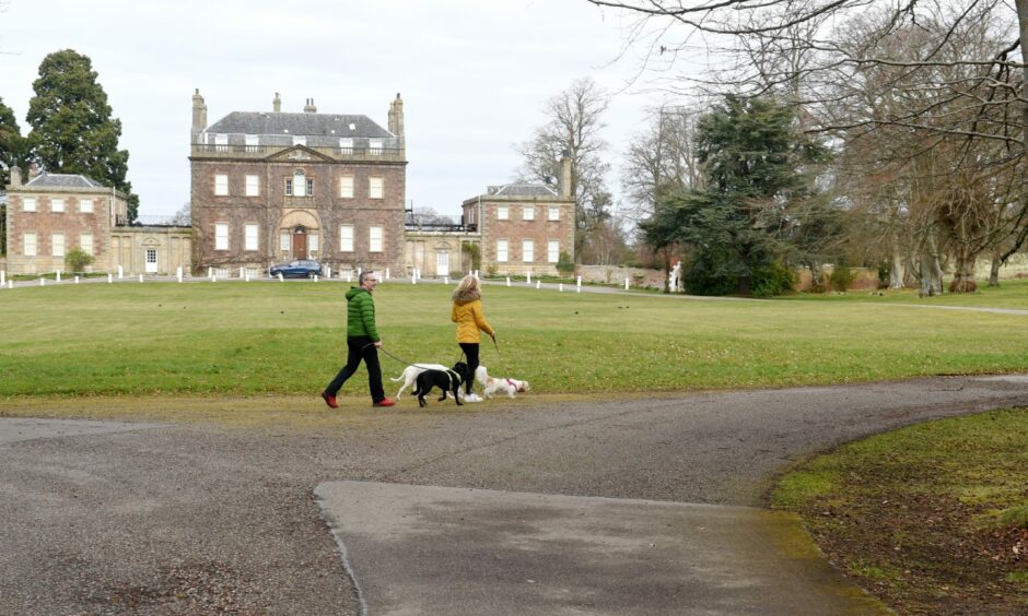 Two people walking dogs on the grounds of Culloden House Hotel