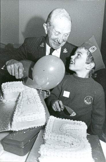 A man and a young boy holding a cake slice each smiling at each other with two cakes in the shape of a 7 and 5.